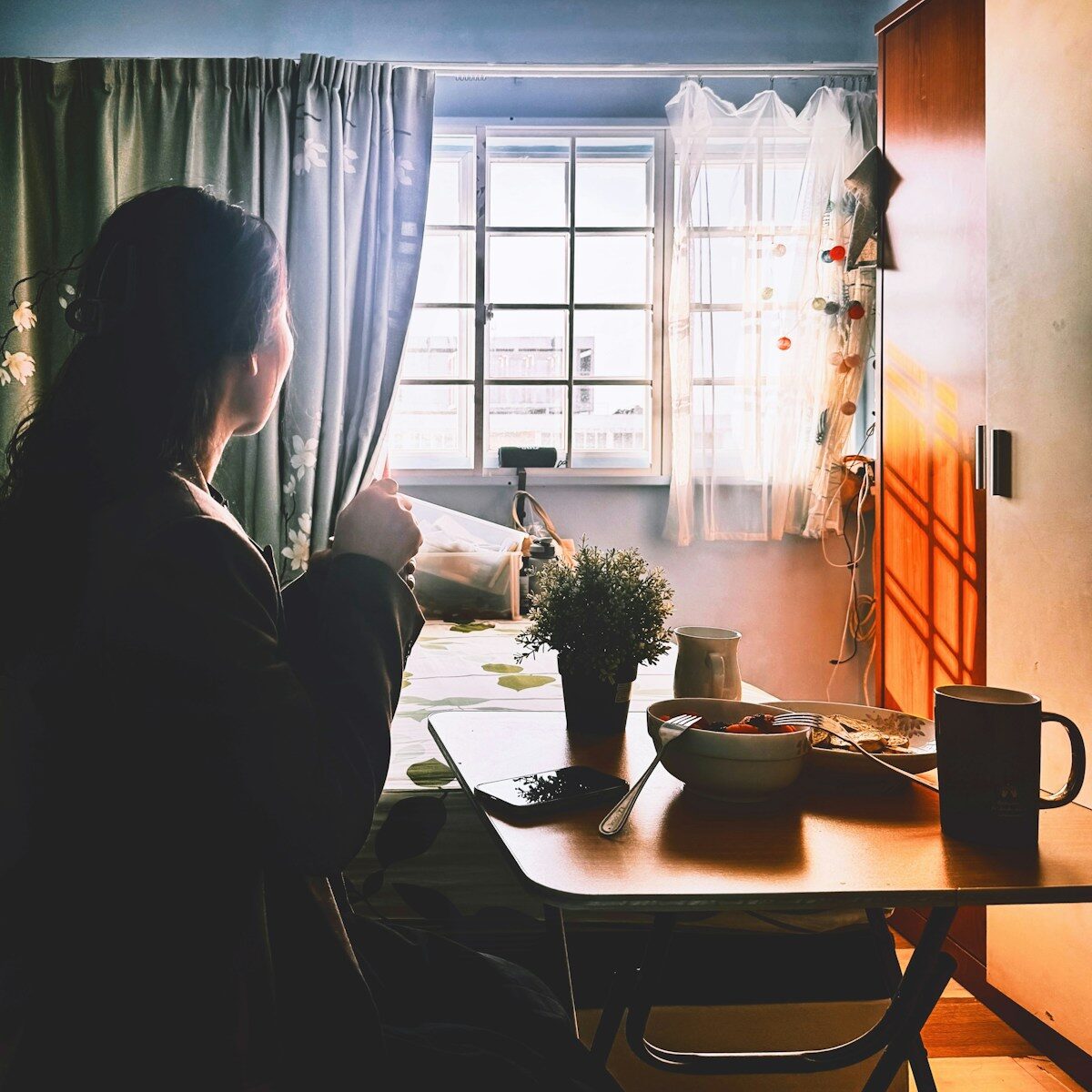 Woman enjoying morning coffee by window light.