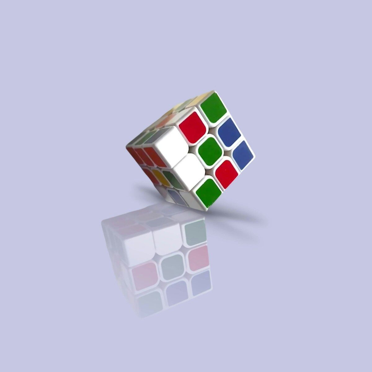 Tilted rubik's cube reflecting on a smooth purple surface.