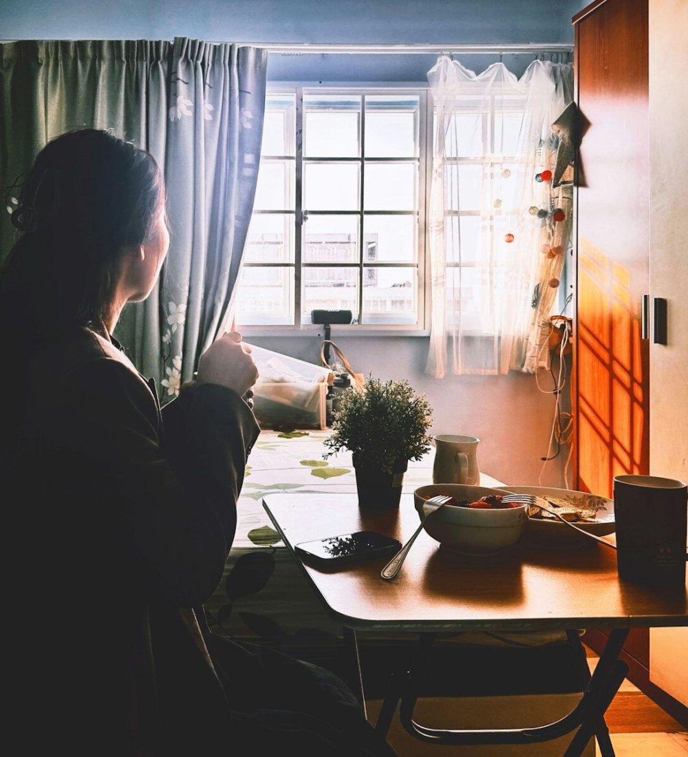 Woman enjoying morning coffee by window light.